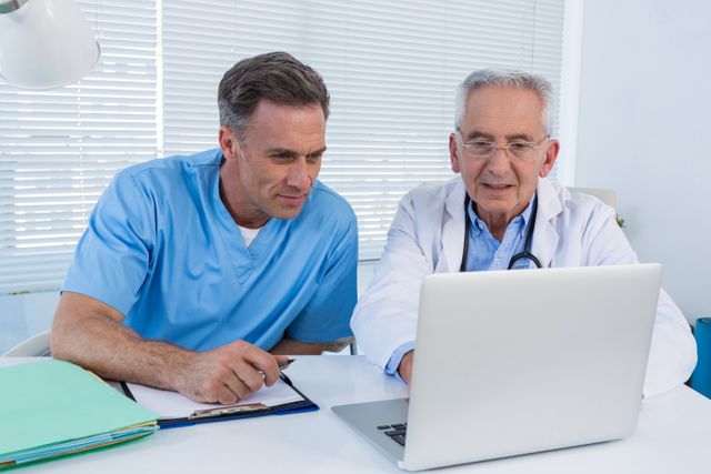 Surgeon and doctor are collaborating and discussing patient records on a laptop in a clinic. This image is ideal for use in healthcare-related articles, medical websites, and promotional materials for clinics and hospitals. It highlights teamwork, professional consultation, and the use of technology in modern healthcare settings.