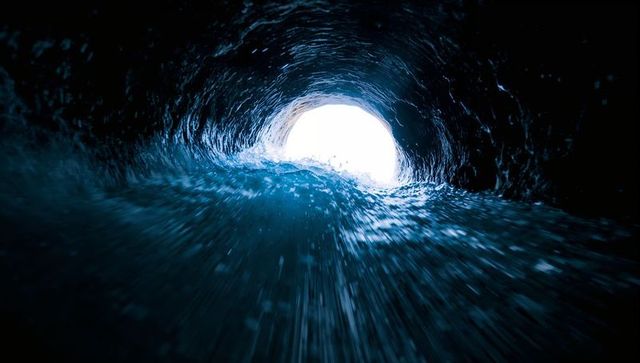Surging inside hollow ocean wave barrel revealing bright circular exit with spray motion