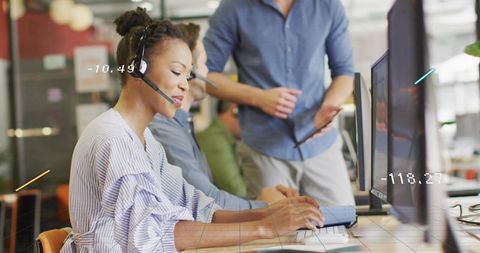 Typing support agent wearing headset and blouse at keyboard in modern open-plan office