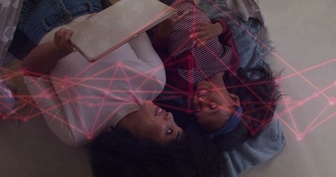 Mother and daughter lying head-to-head sharing tablet, bonding with digital network overlay