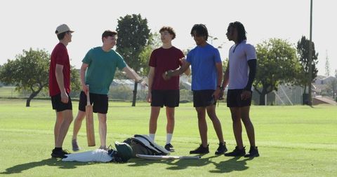 Diverse teen teammates gathering for cricket pregame huddle on sunny grass field, bonding