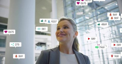Smiling businesswoman standing in modern atrium surrounded by social media notifications
