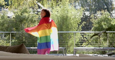 Joyful Woman Embracing Rainbow Pride Flag on Sunny Terrace
