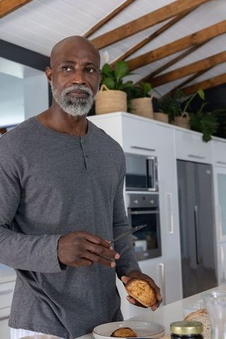 Senior african man slicing roasted potato at kitchen island preparing healthy home breakfast
