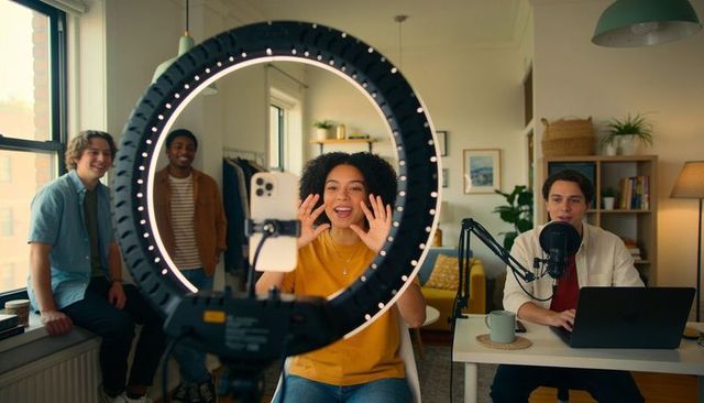Young creators hosting live stream using ring light, podcast mic, laptop in cozy apartment
