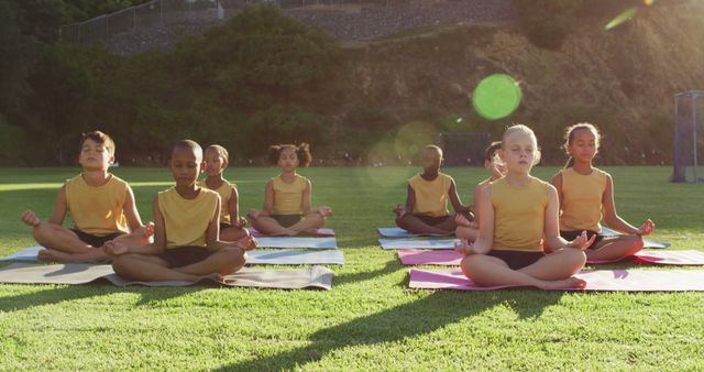 Diverse group of schoolchildren sitting on mats meditating during yoga lesson outdoors. children at primary school in summer.