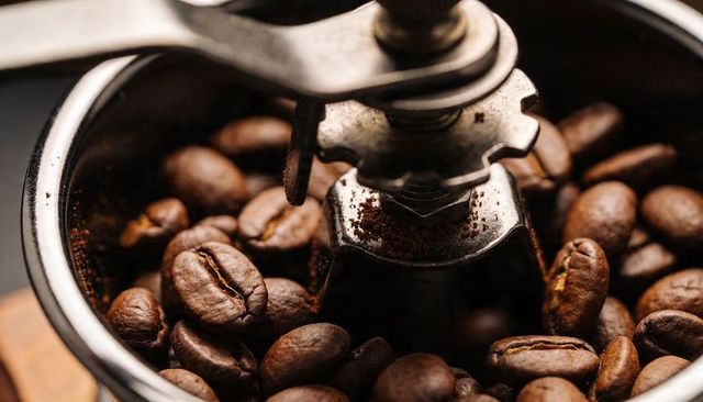 Manual coffee grinder burr amid roasted beans showing fresh grounds and rustic texture