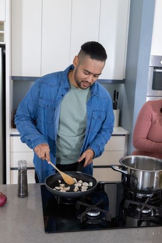 Couple cooking together in modern kitchen man stirring mushrooms with wooden spatula