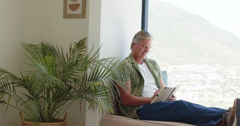 Mature man reviewing isometric vector blueprint on tablet while relaxing by window