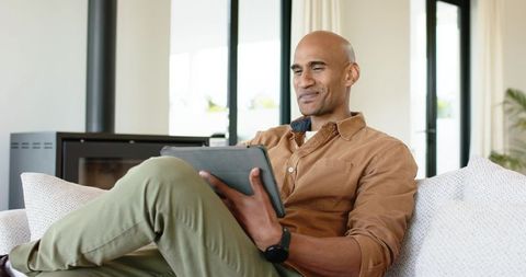 Mature african american man relaxing on sofa using tablet in modern sunlit home