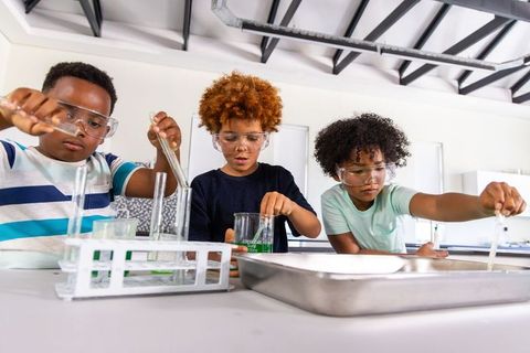 Multiracial school boys conducting hands-on chemistry experiment wearing safety goggles