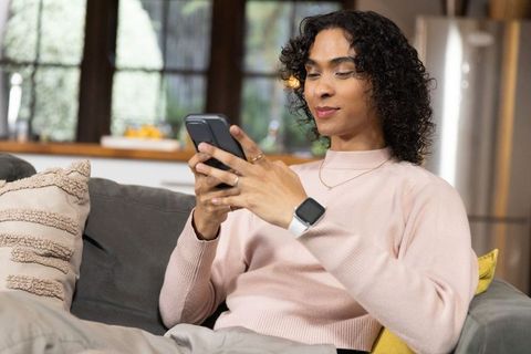 Non-binary person relaxing on sofa and texting with smartwatch in modern living room