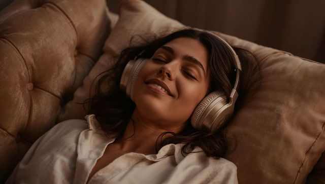 Woman relaxing with headphones on tufted sofa, cozy warm lifestyle listening scene