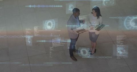 Coworkers discussing augmented reality data with laptop and tablet in modern atrium