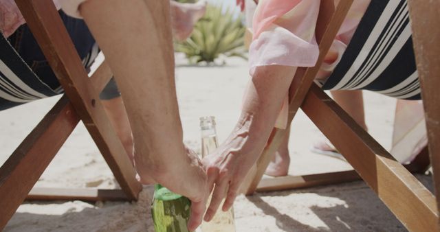 Couple sitting in beach chairs enjoying a sunny day and reaching for drinks. Ideal for travel agencies promoting beach vacations, lifestyle articles focusing on summer relaxation, or advertisements for refreshing beverages. Highlights leisure and relaxation.