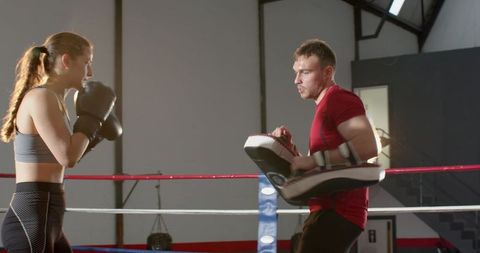 Female boxer training with coach holding focus pads in boxing ring, intense workout