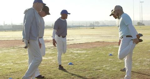 Adult baseball team warming up with stretching and coaching on morning practice field