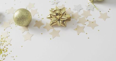 Gold gift bow with glitter bauble and star confetti on white tabletop holiday celebration