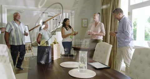 Multigenerational friends laughing and pouring wine around dining table during home gathering