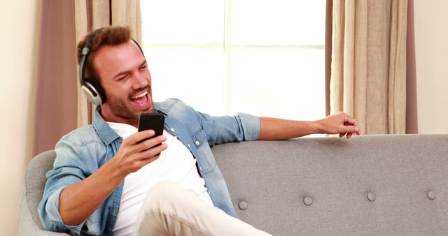 Handsome man listening to music and using smartphone on the sofa - Download Free Stock Photos Pikwizard.com