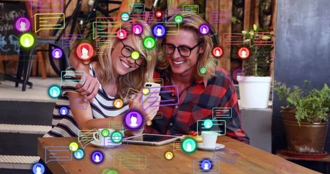 Smiling couple sharing smartphone and browsing social feeds in cozy cafe with chat icons