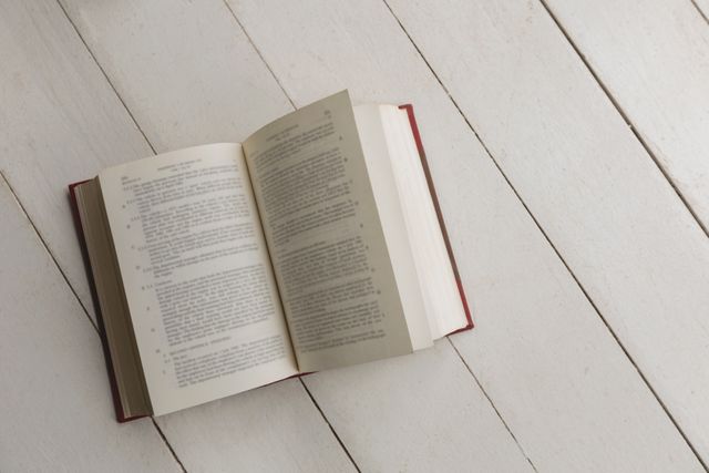 This image shows an open book placed on a wooden floor, suggesting a quiet and peaceful environment for reading or studying at home. It can be used for themes related to literature, education, relaxation, and home decor. Ideal for websites, blogs, or advertisements focusing on books, learning, or cozy home settings.