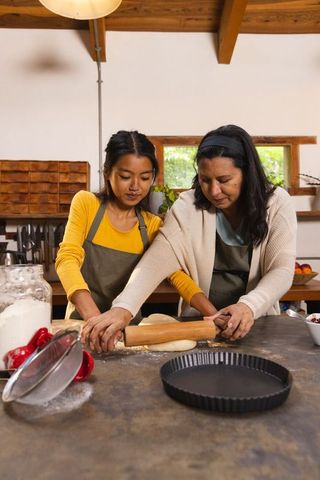 Diverse mother and daughter rolling pastry in home kitchen