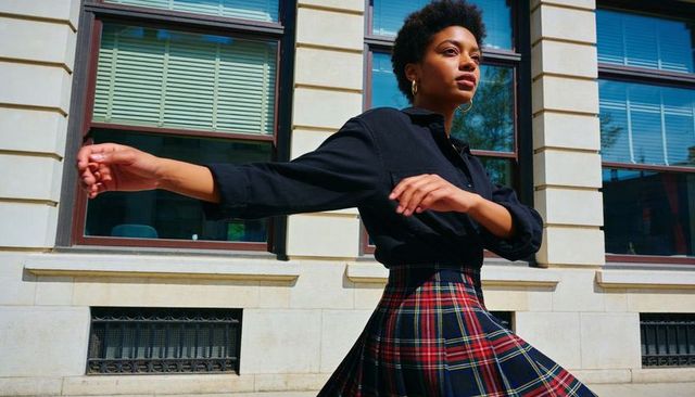 Young woman walking urban street turning in black shirt and tartan plaid skirt