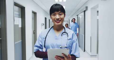 Smiling asian female doctor in hospital corridor with tablet