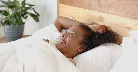 Woman Relaxing in Bed with White Duvet Smiling Joyfully