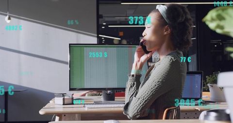 Businesswoman talking on smartphone while checking spreadsheet at modern office workstation