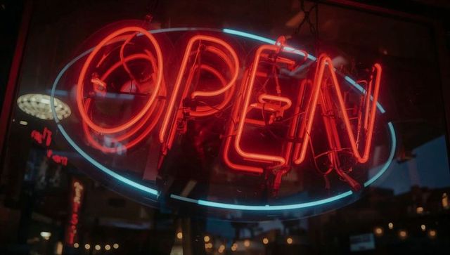 Neon open sign glowing red and blue reflecting on storefront glass with visible wiring