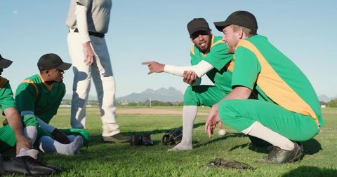 Multicultural baseball team huddling and practicing on grass with coach giving instructions