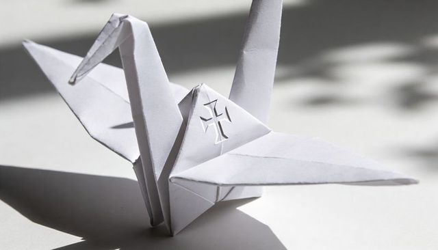 Origami crane with cross cutout casting sharp shadow on minimal white surface