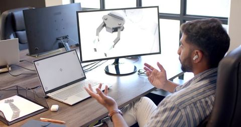 Indian engineer gesturing and explaining 3D robotic gripper design on monitor
