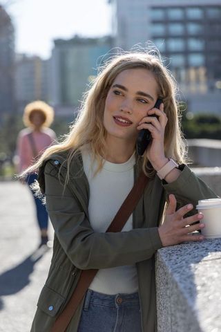 Young woman talking on smartphone while leaning on urban railing with takeaway coffee