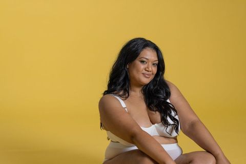 Confident plus size woman modeling white lingerie on warm golden backdrop, relaxed pose