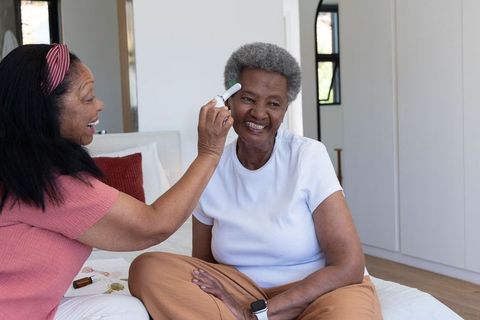 African american caregiver checking senior woman with forehead thermometer at home