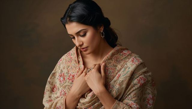 Serene woman adjusting embroidered beige shawl wearing elegant jewelry