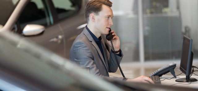 Side view of salesman talking on landline phone in car showroom