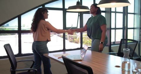 Two Female Colleagues Shaking Hands in Modern Conference Room With Laptop During Daylight Meeting