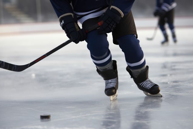 Hockey players skating on ice rink, focused on puck during action-packed game. Captures dynamic movement in winter sport. Use for sports articles, winter sports promotions, or team apparel marketing.