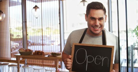 Smiling Waiter Welcoming Customers in Cozy Cafe with Open Sign - Download Free Stock Images Pikwizard.com
