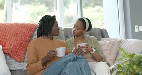 African American couple sharing coffee on cozy sunlit sofa with knit throw and plant