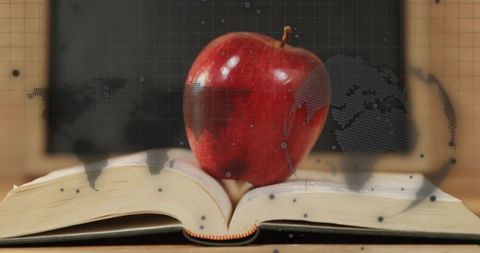 Red Apple Balancing on Book with World Map Overlay in Classroom