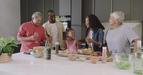 Multigenerational family at modern kitchen island preparing healthy salad and sharing laughter