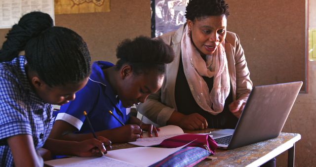 female teacher helping students with laptops in classroom setting - Download Free Stock Images Pikwizard.com