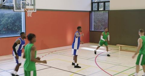 Diverse male basketball players driving for layup and shaking hands, teamwork indoor court