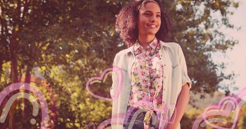 Joyful woman in sunlit park with heart rainbow overlays