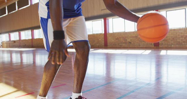 Image illustrates a male athlete dribbling basketball on an indoor court. The athlete is wearing a sports uniform and wristbands. This stock photo is suitable for sports blogs, fitness articles, training tutorials, and advertisements for sportswear or gym memberships.